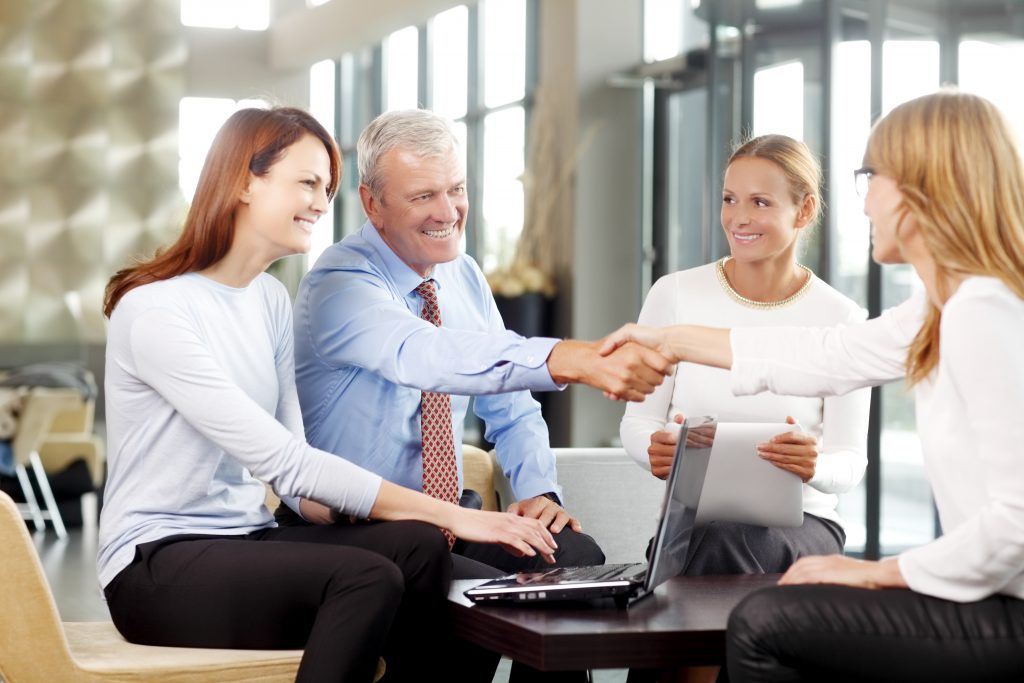 Old businessman shaking hands with confident business woman at meeting.